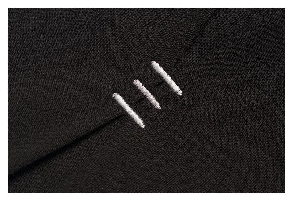 Close-up of three short white embroidered bars on black fabric.