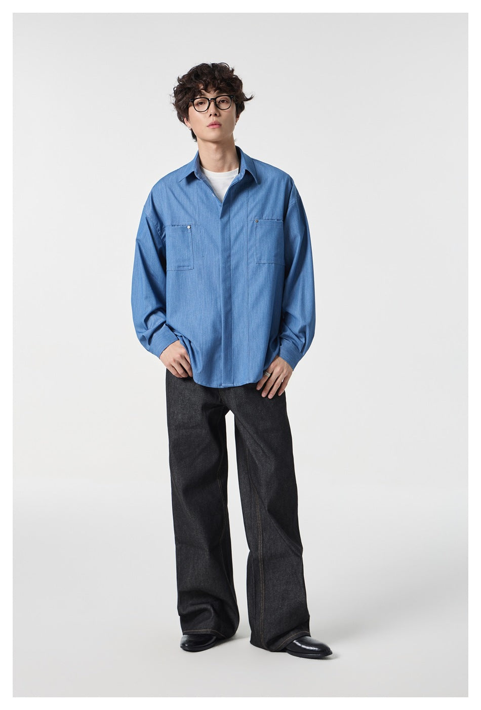 Full-length model wearing an oversized blue button-up shirt with two chest pockets over a white tee and dark wide-leg jeans.