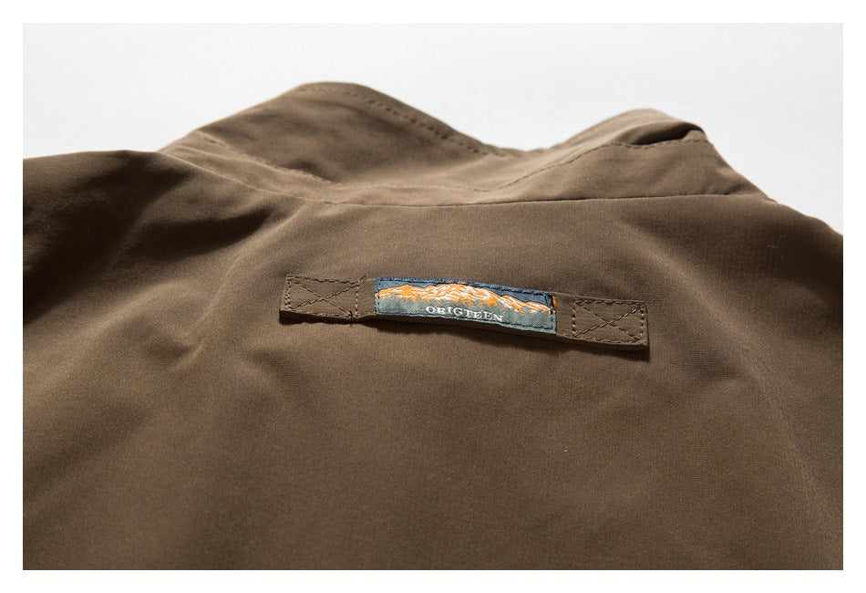 Close-up of a small embroidered ORIGREEN label stitched onto brown jacket fabric.