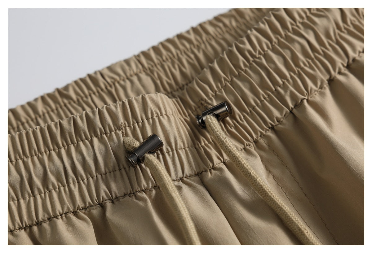 Close-up of tan garment's gathered elastic waistband with braided drawstrings and dark metal cord locks.