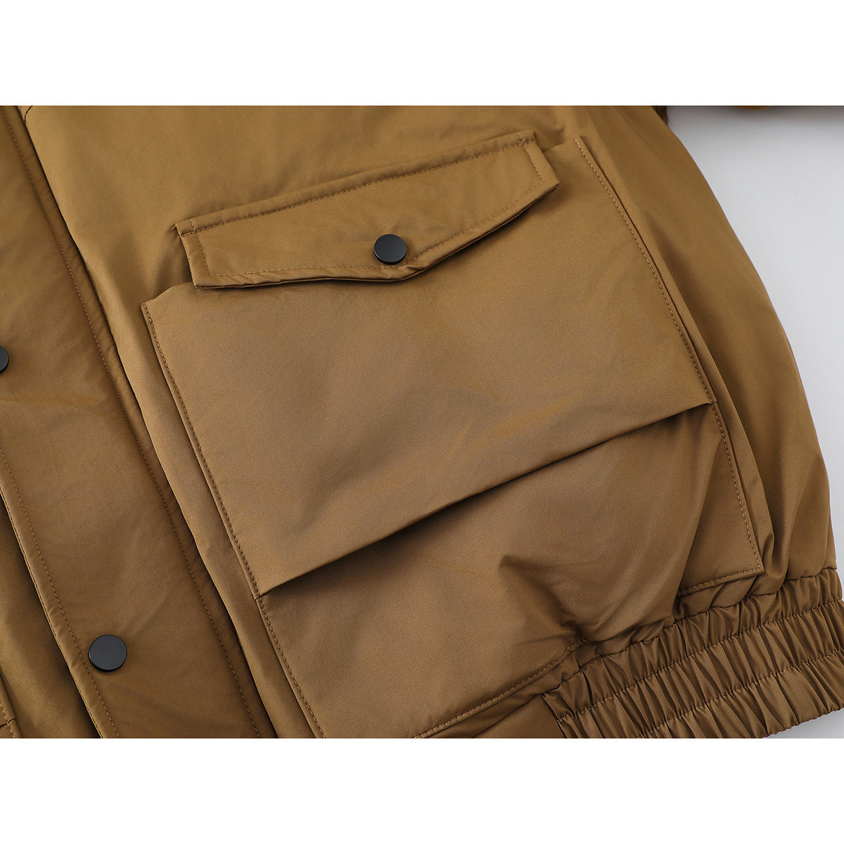 Close-up of a camel-brown jacket showing a large flap pocket, black snap, and gathered hem.