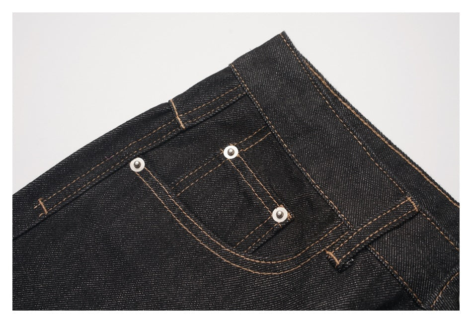 Close-up of a small front coin pocket with metal rivets and tan stitching on dark denim jeans.