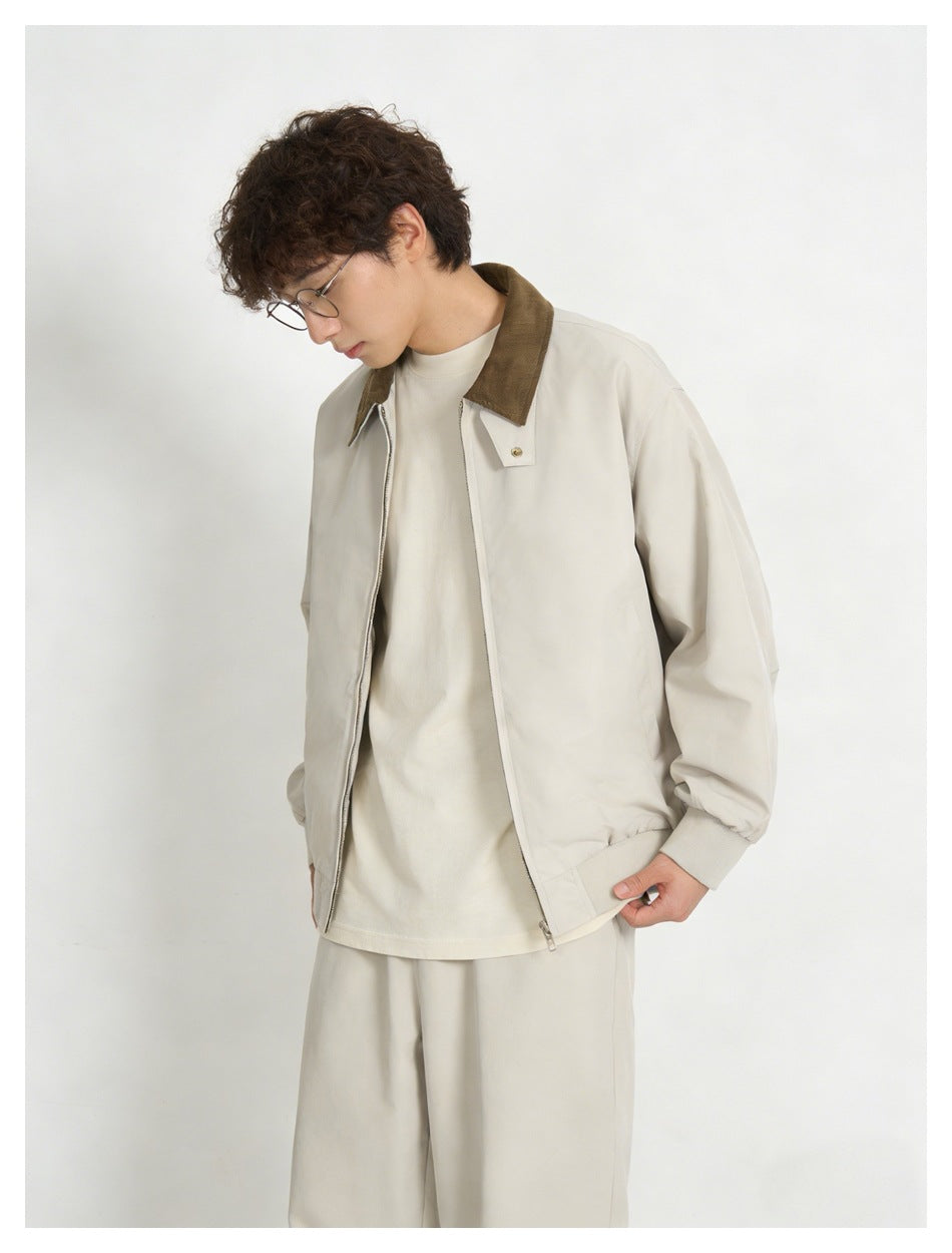 Model looking down while wearing a light cream zip jacket with a brown collar and matching trousers.