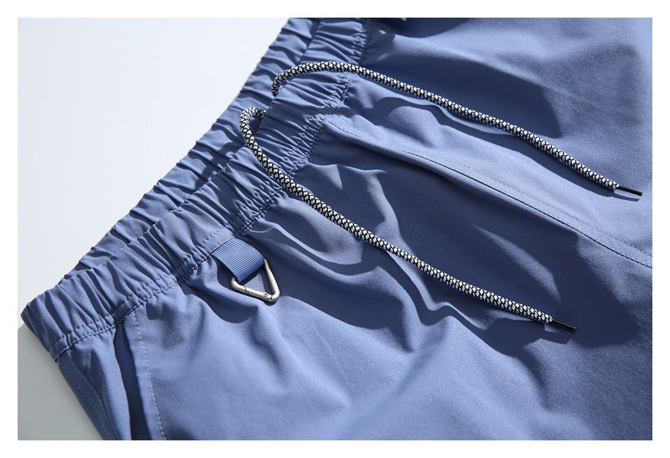 Close-up of blue shorts showing the elastic waistband, drawcord, metal loop, and a zippered pocket.