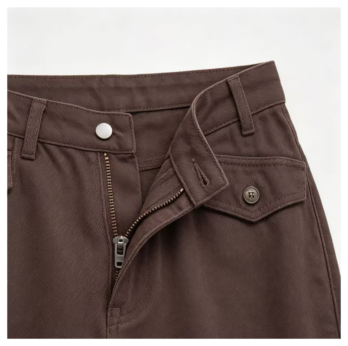 Close-up of the brown trousers' waistband, button, open zipper fly, and flap pocket.