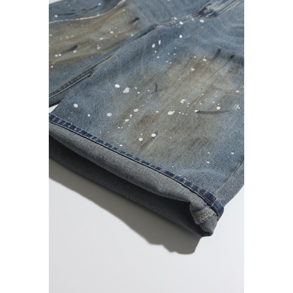 Close-up of a rolled jeans hem with white paint splatters and faded, distressed blue denim.