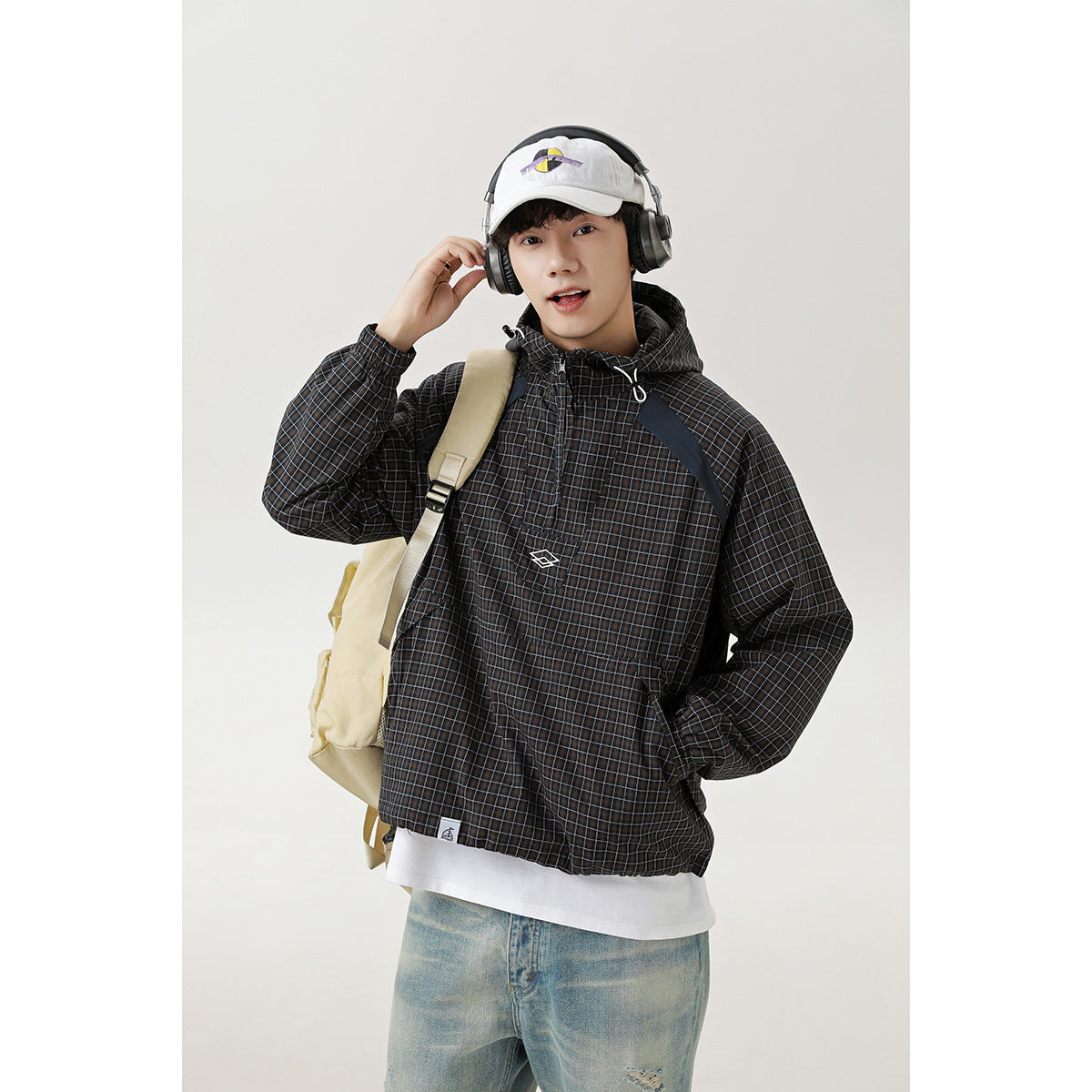 Man wearing a black checked hooded pullover jacket with a front pocket and drawstrings, styled with jeans and a backpack.