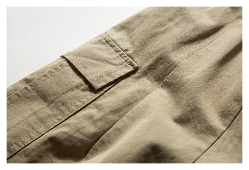 Close-up of a tan trouser leg with a buttonless flap cargo pocket and visible stitching.