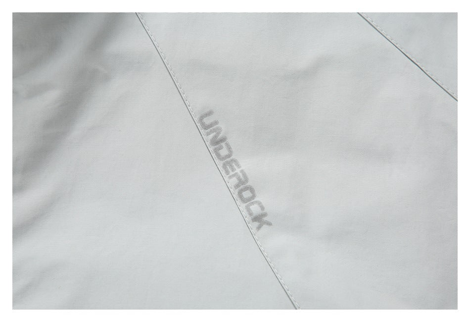 Close-up of a light gray garment with tonal UNDEROCK lettering beside a stitched seam.