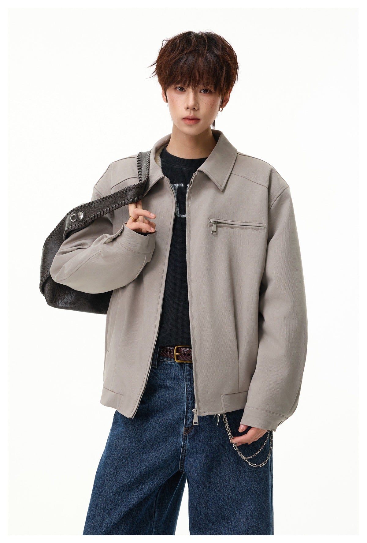 Model wearing a light taupe zip jacket with a pointed collar and chest zip pocket, carrying a dark shoulder bag.