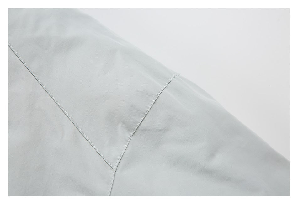 Close-up of a light gray garment showing intersecting stitched seams and a shaped panel.