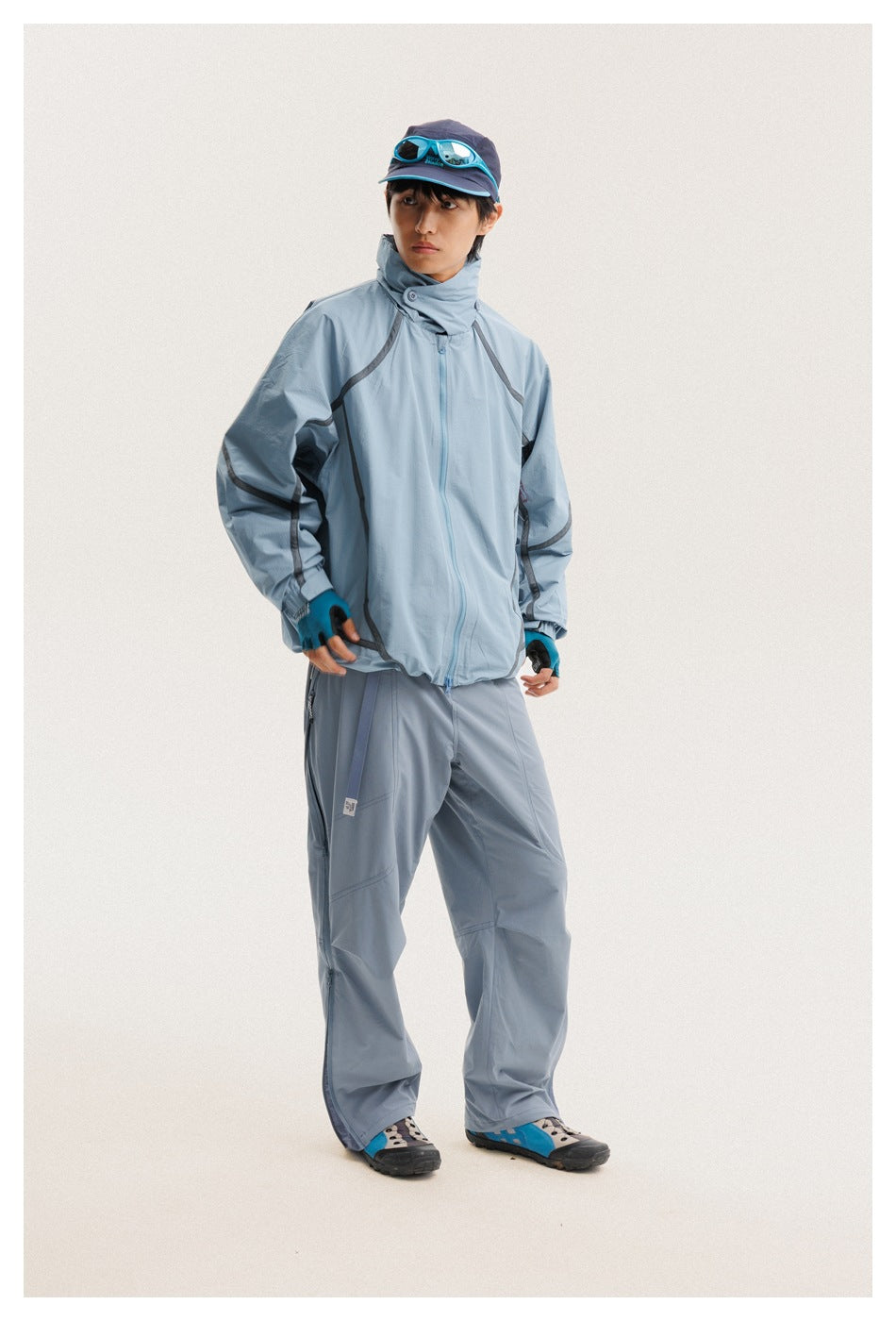Front view of a model wearing a pale blue zip jacket with dark curved trim and matching pants.