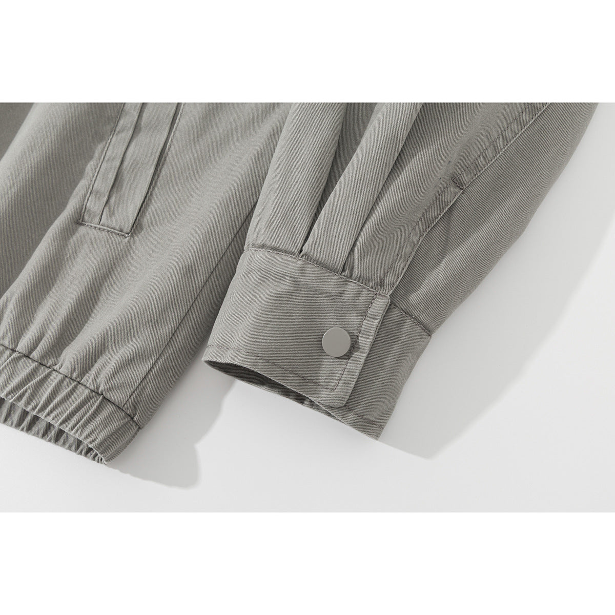 Close-up of a gray jacket sleeve cuff with a snap button and gathered hem nearby.