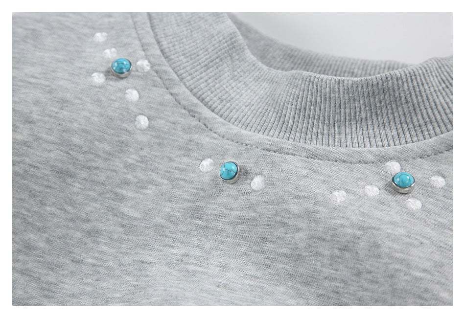 Close-up of a ribbed crew neckline and turquoise buttons among white stitched dots on a heather gray sweatshirt.