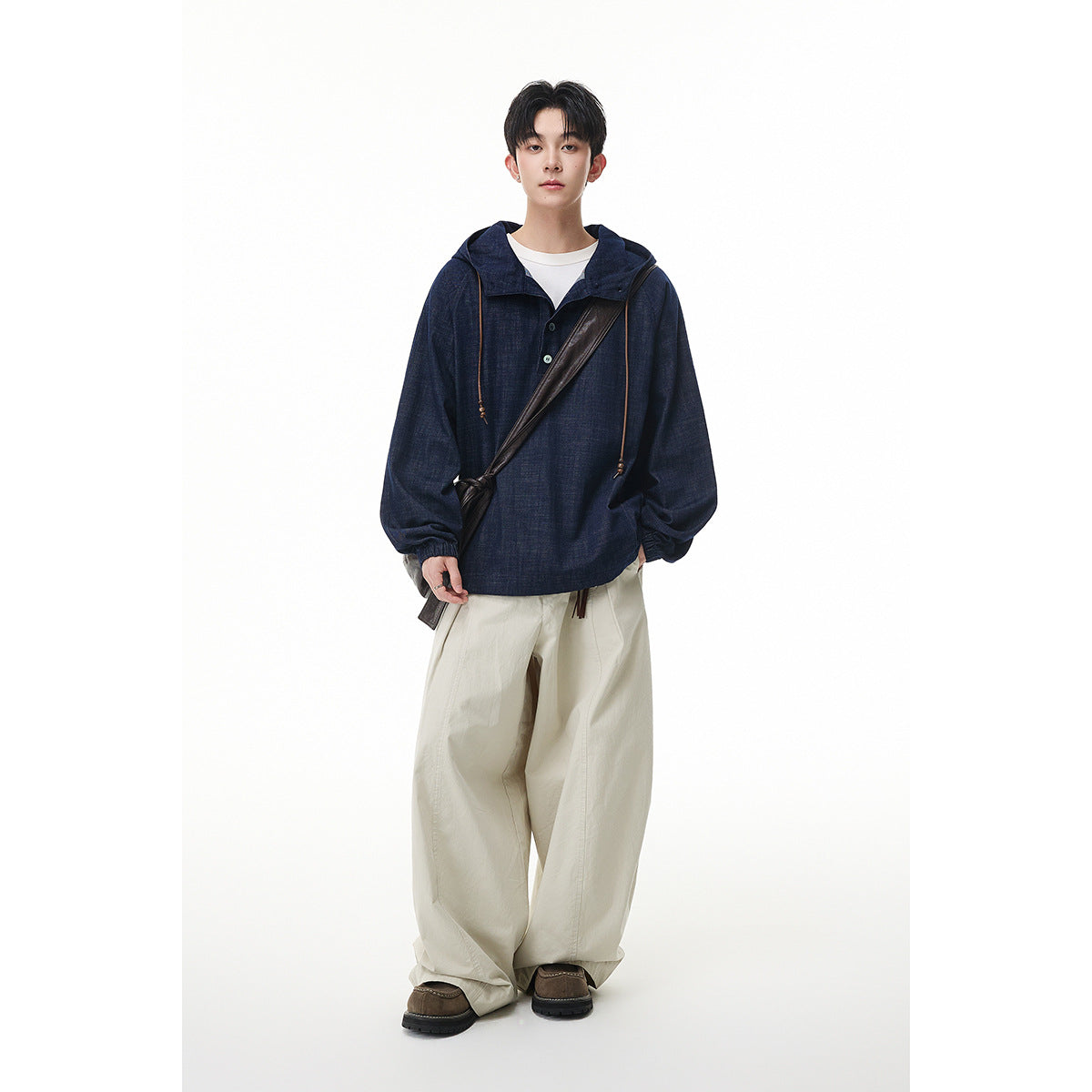 Full-length model wearing a navy hooded pullover over a white shirt, cream wide-leg trousers, and a dark crossbody bag.