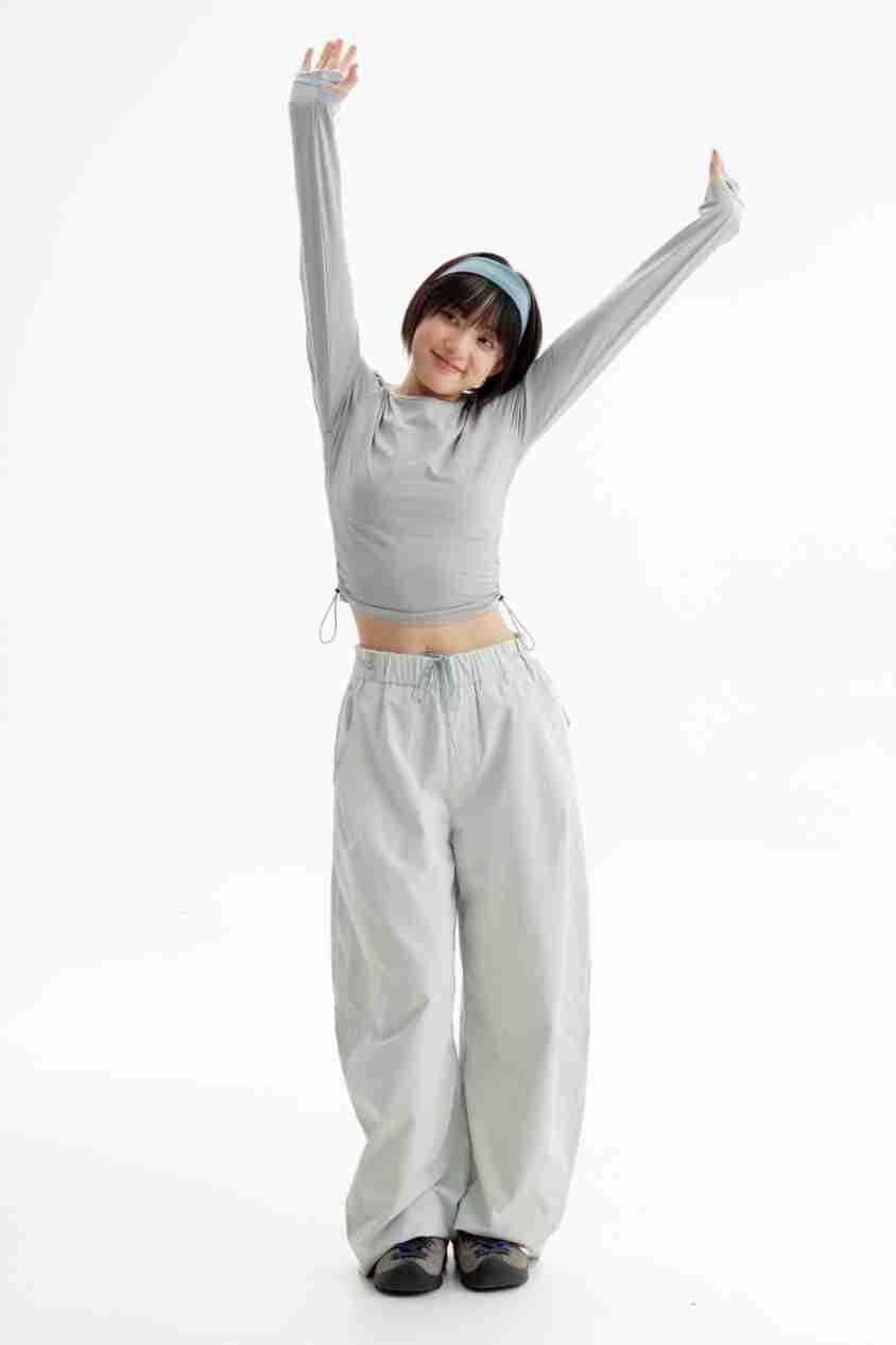 Model wearing a gray cropped long-sleeve top and loose pale gray pants, posing with both arms raised.