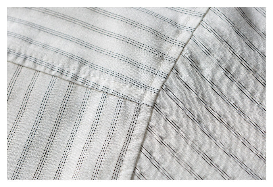 Close-up of light gray fabric with fine dark stripes and intersecting stitched seams.
