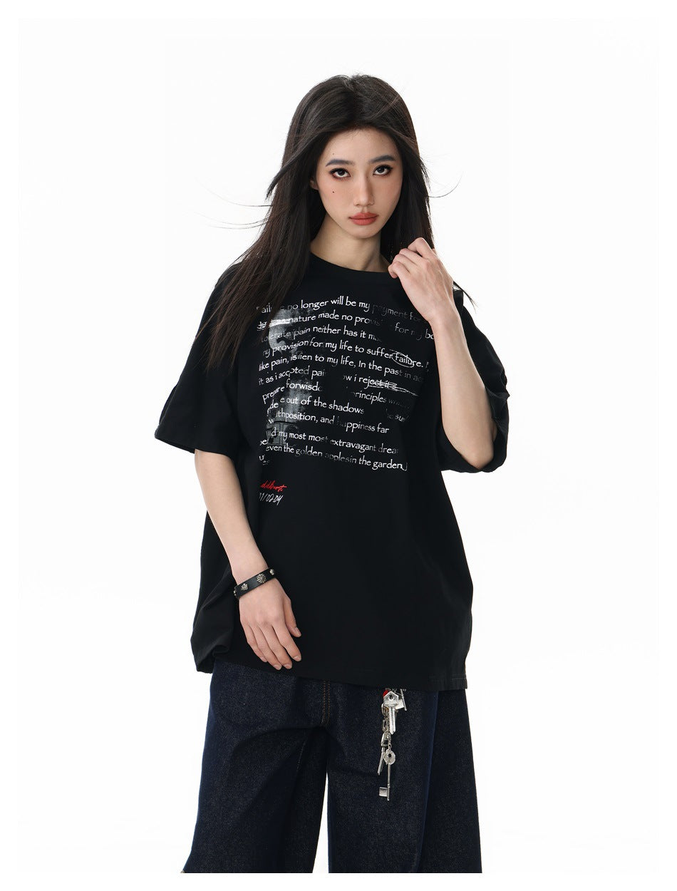 Model in the black oversized text-print t-shirt with dark denim bottoms, close-up three-quarter view of the front print