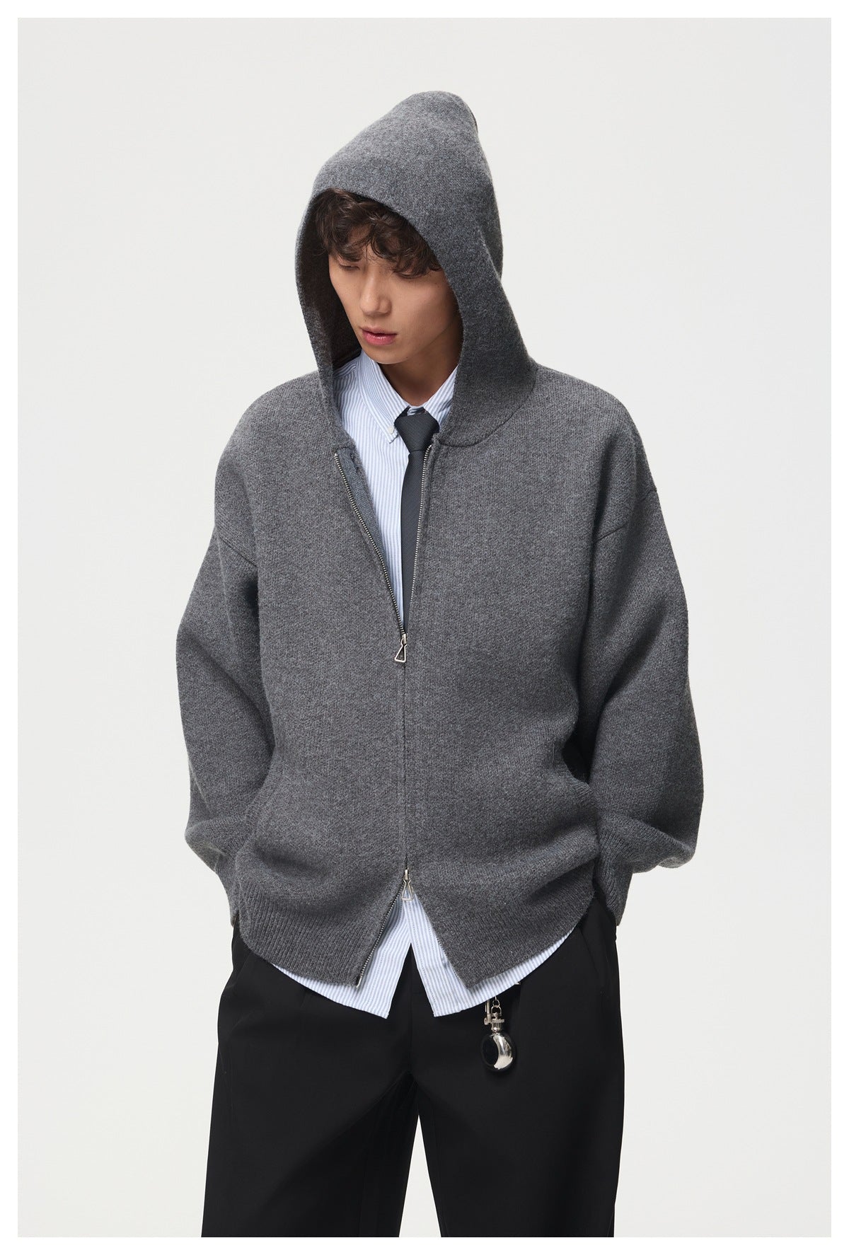 Model wearing a charcoal gray zip-front hooded cardigan with the hood up, layered over a striped shirt and tie.
