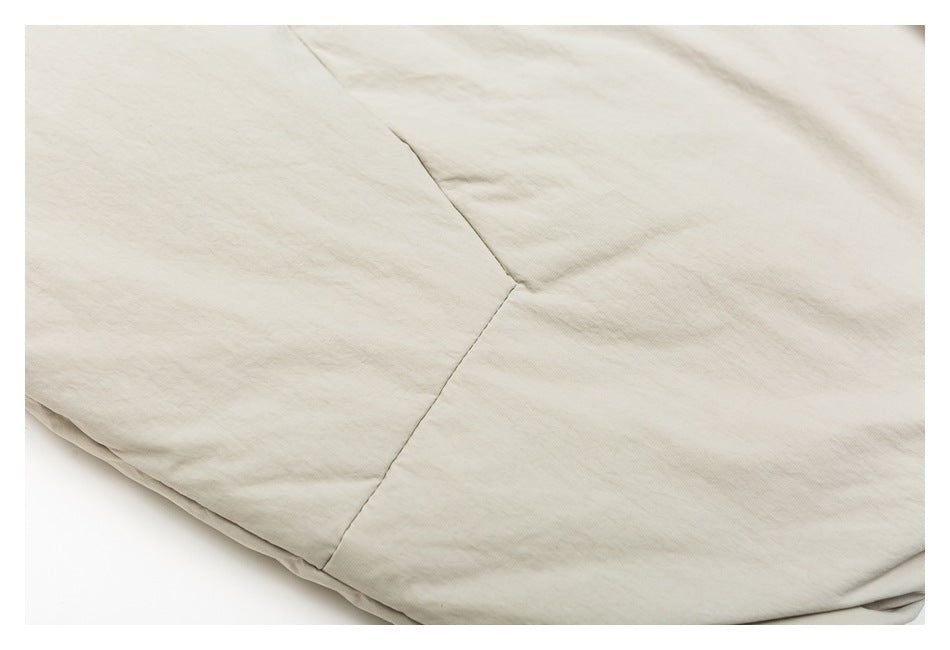 Close-up of pale beige garment fabric showing a joined seam and softly creased surface.