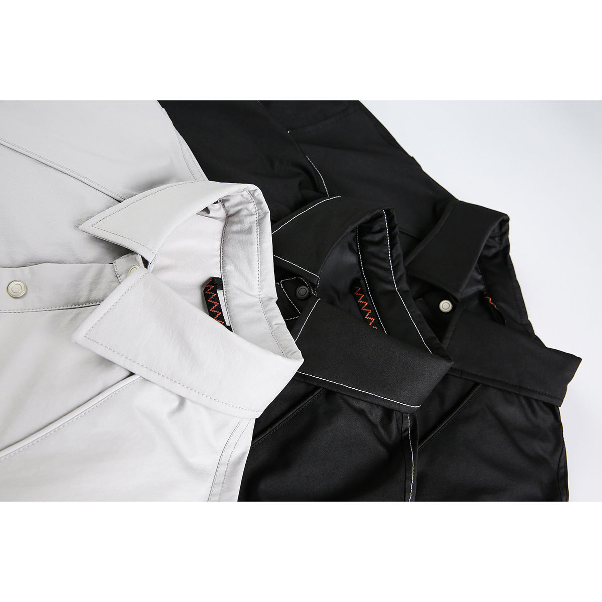 Close-up of light gray and black jackets showing pointed collars, snap details, contrast stitching and trim.