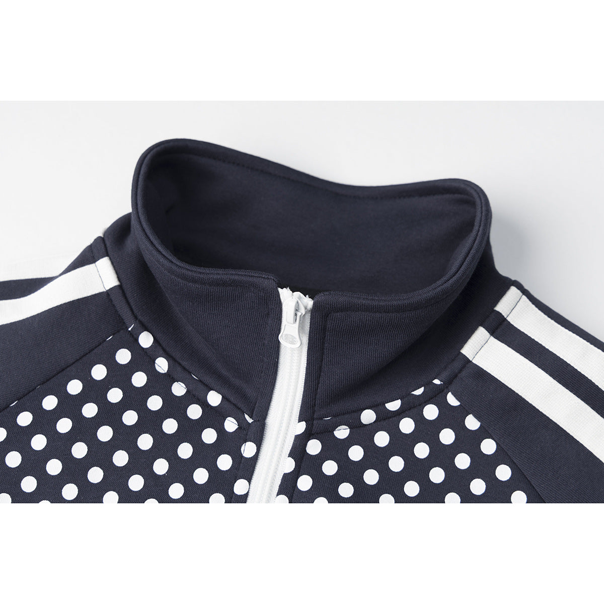 Close-up of a navy track jacket's raised collar, white zipper, shoulder stripes, and white polka-dot panels.