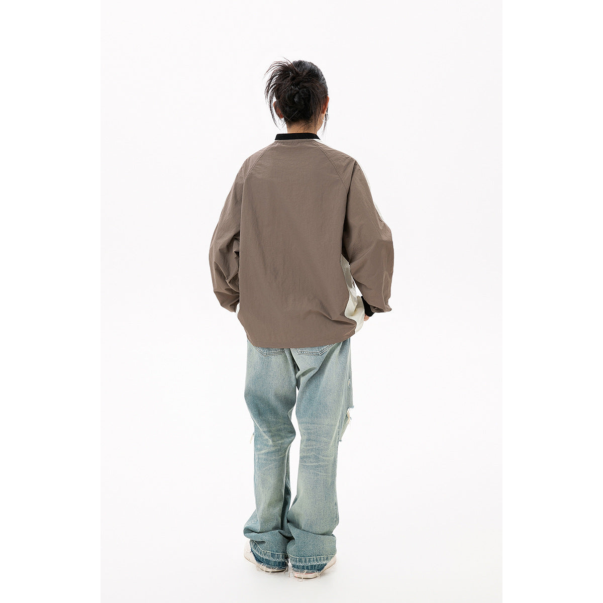 Rear view of a model wearing a taupe pullover with cream side panels, black collar and cuffs.