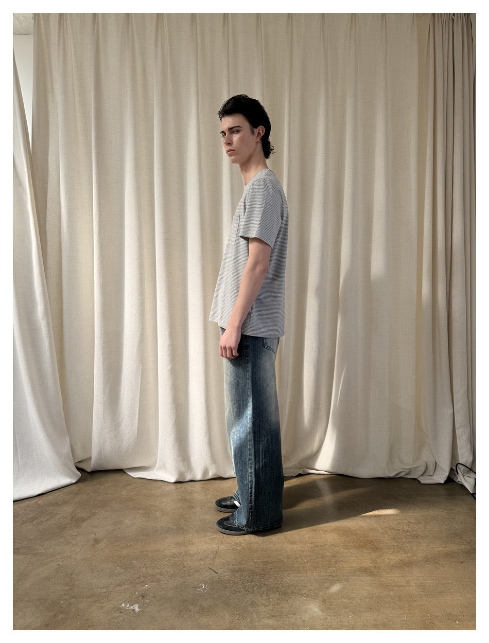 Model in side view wearing a gray-and-white striped short-sleeve T-shirt and faded wide-leg blue jeans.