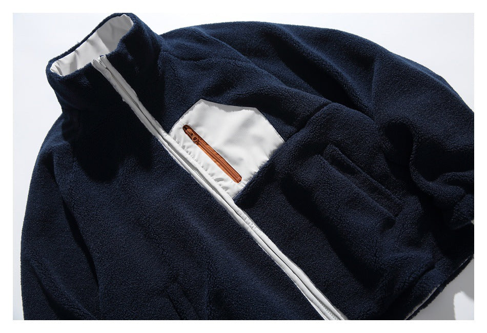 Partial flat lay of a dark navy fleece jacket with a high collar, white front zipper, and contrasting chest pocket with