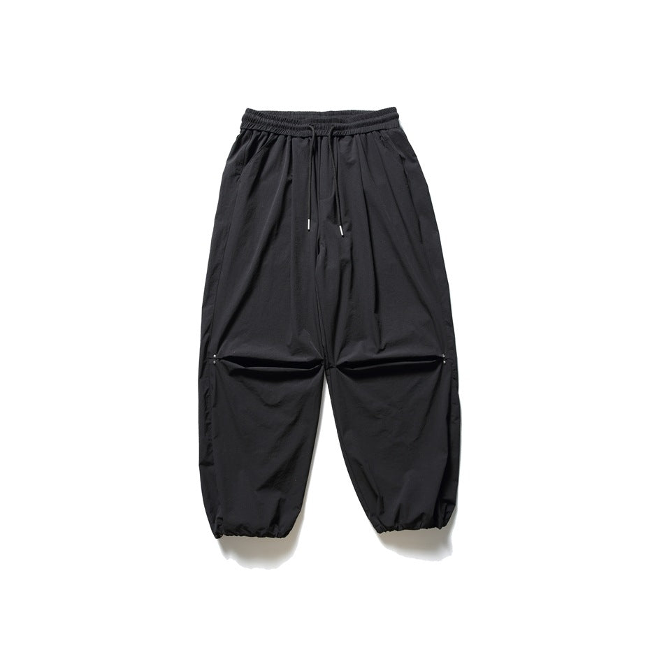 Front view of black wide-leg pants with an elastic drawstring waist, horizontal knee openings and gathered cuffs.