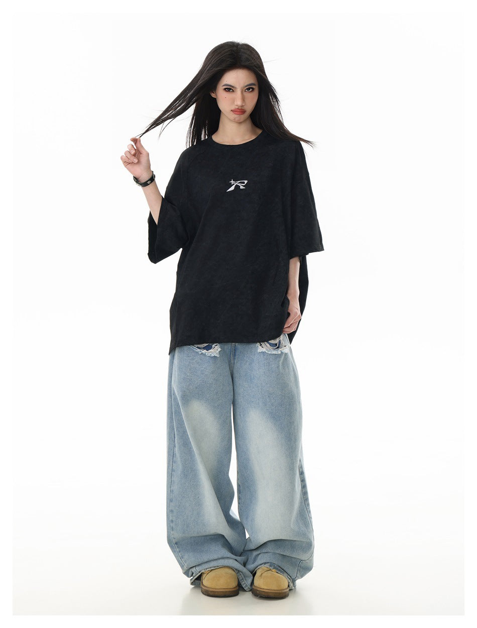Model wearing an oversized black T-shirt with a small white chest emblem and loose light-wash jeans.