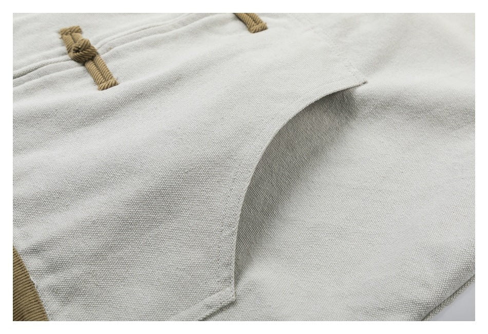 Close-up of light gray fabric with a curved overlapping panel and tan braided loop details.