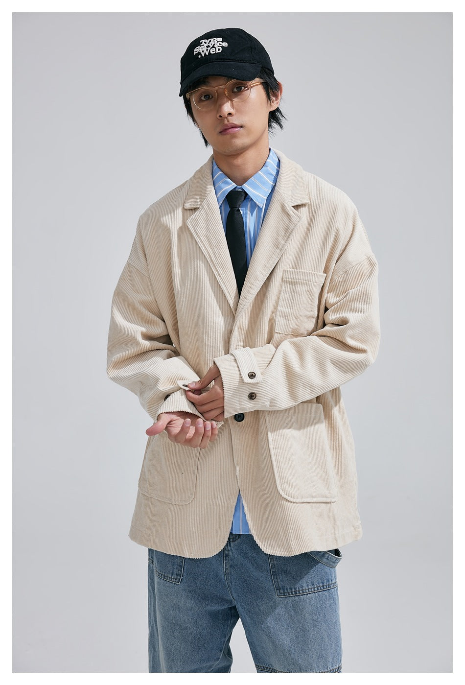 Front view of a model in an oversized cream corduroy blazer with three patch pockets, layered over a blue striped shirt and