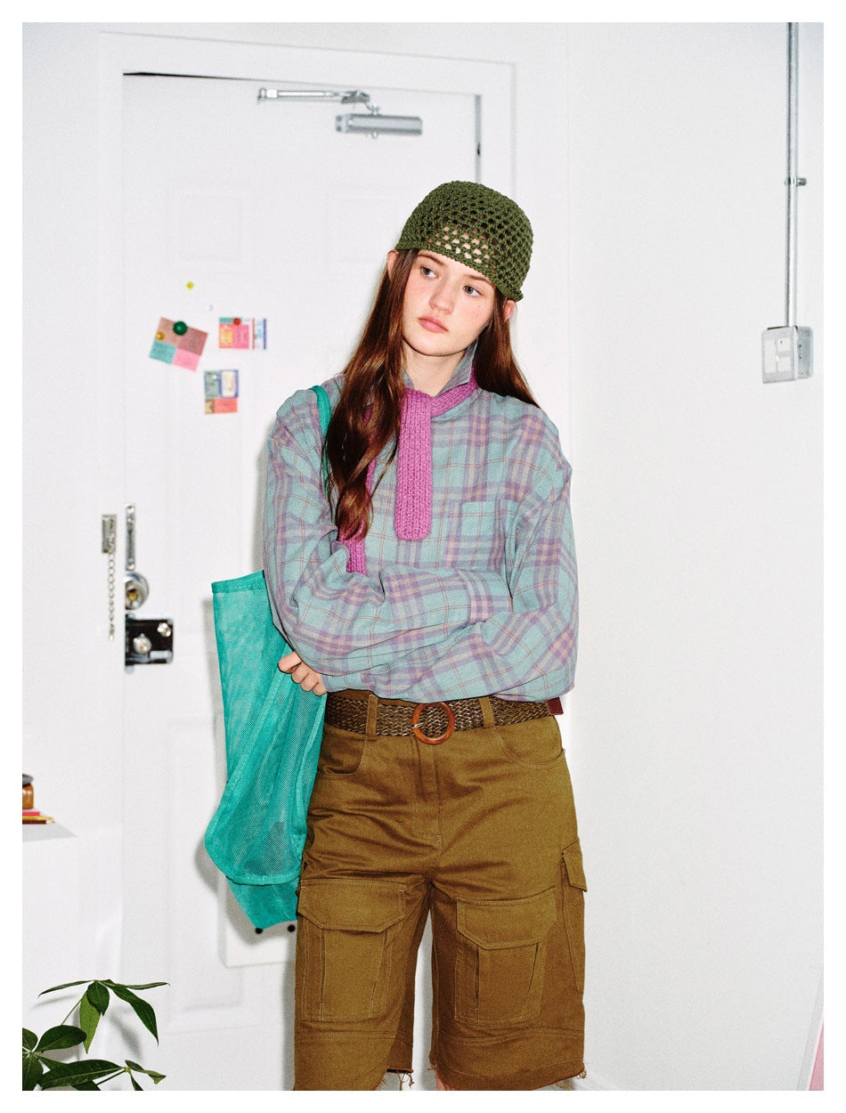 Model with arms crossed wearing the mint and purple plaid shirt with a pink knit scarf, beanie and olive cargo shorts