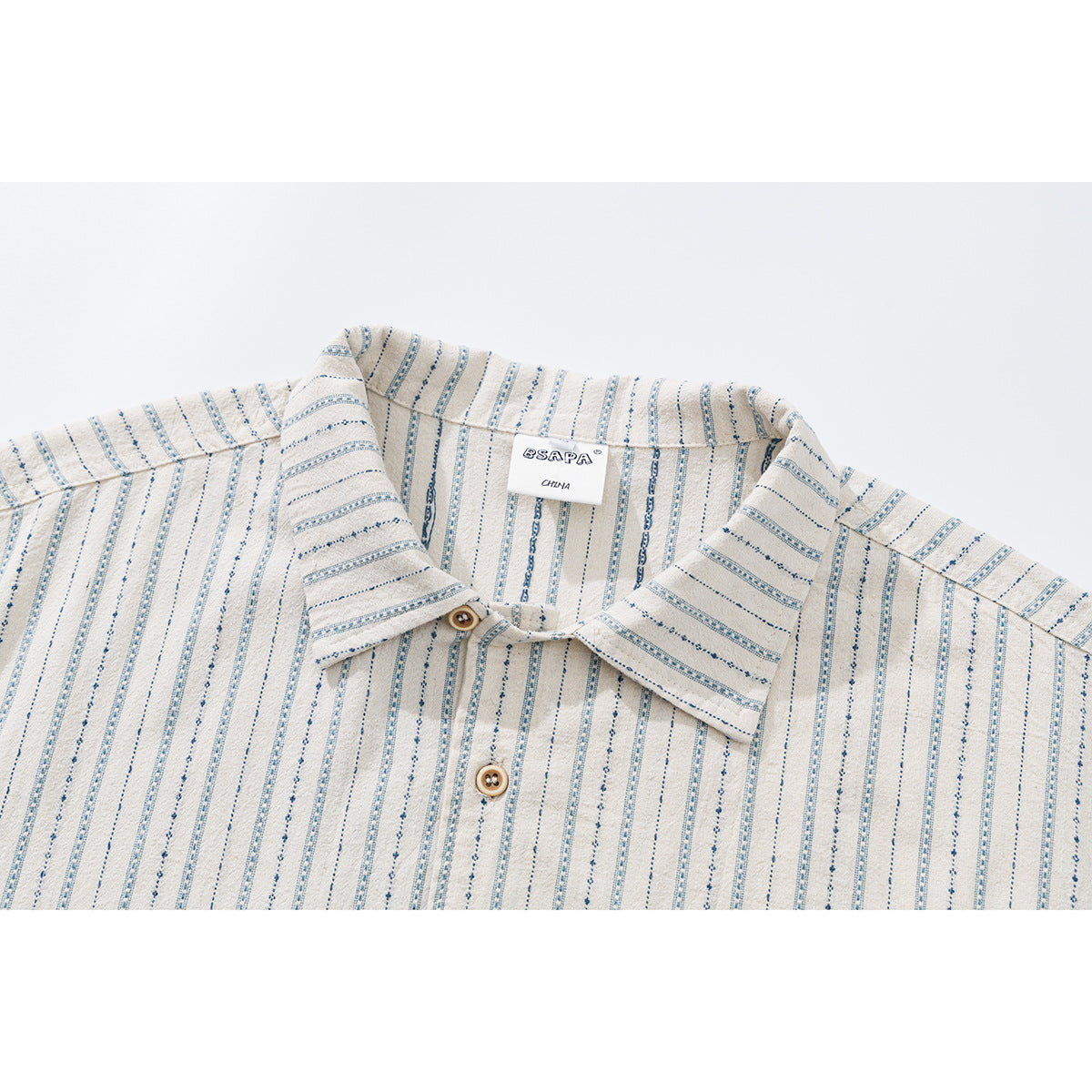 Close-up of a cream short-sleeve shirt collar with narrow blue patterned stripes and tan buttons.