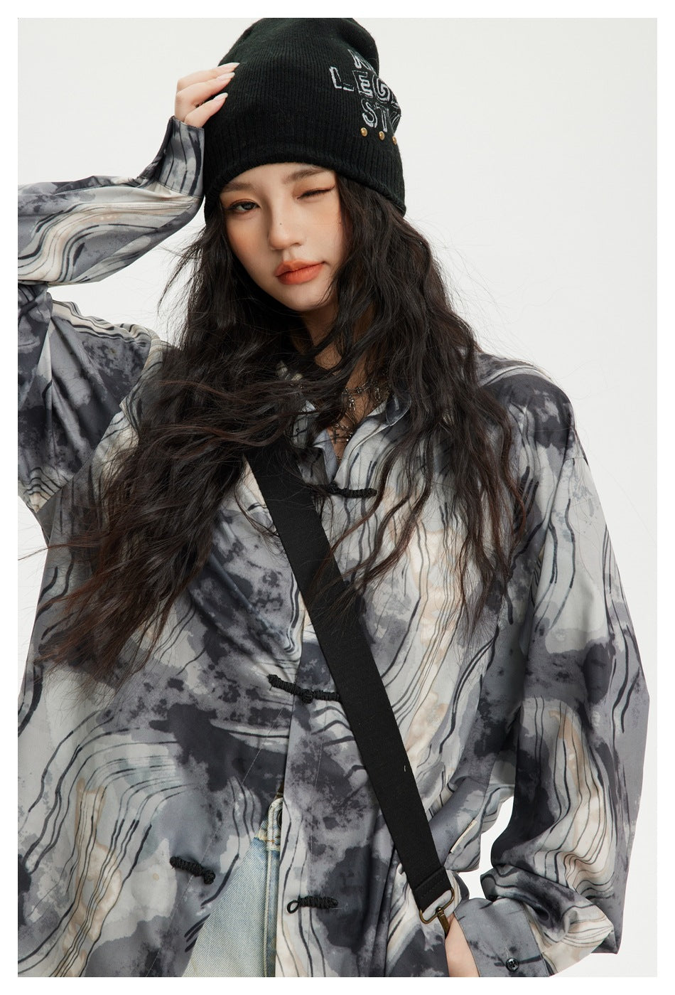 Close view of a model in a gray abstract-print shirt with black frog closures and a black beanie.