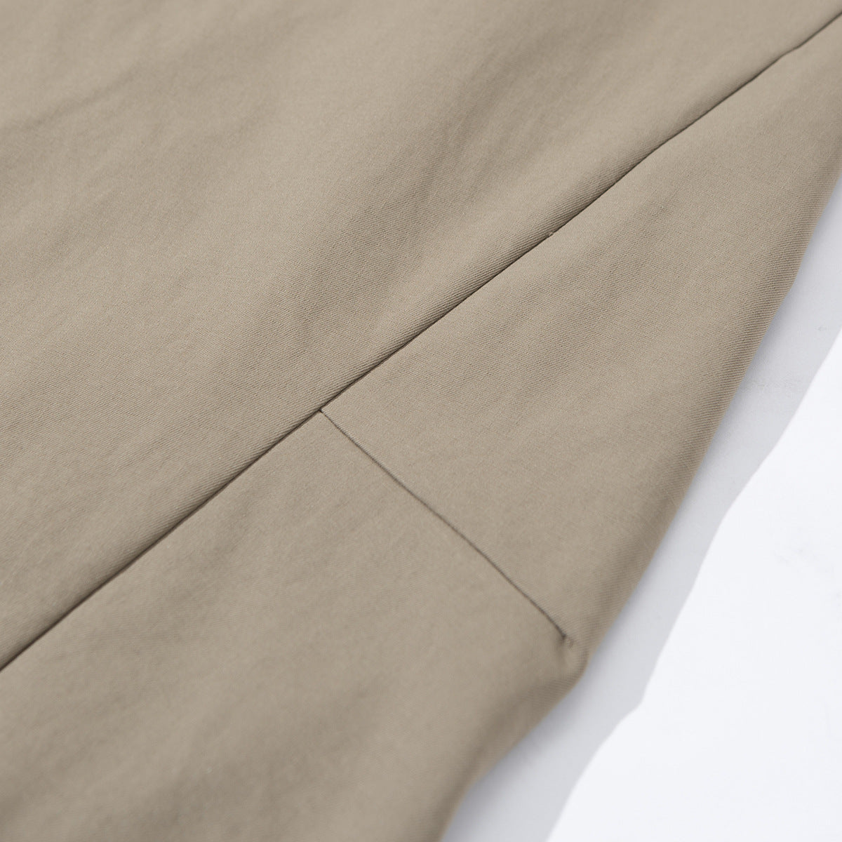 Close-up of taupe trouser fabric with a diagonal seam and hem stitching.