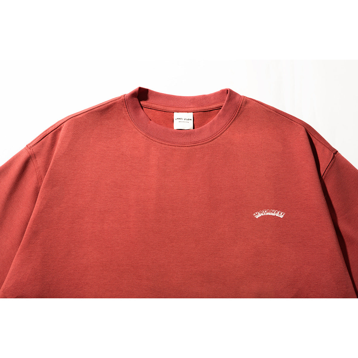 Close-up of a muted red crew-neck T-shirt with a small white arched chest emblem.