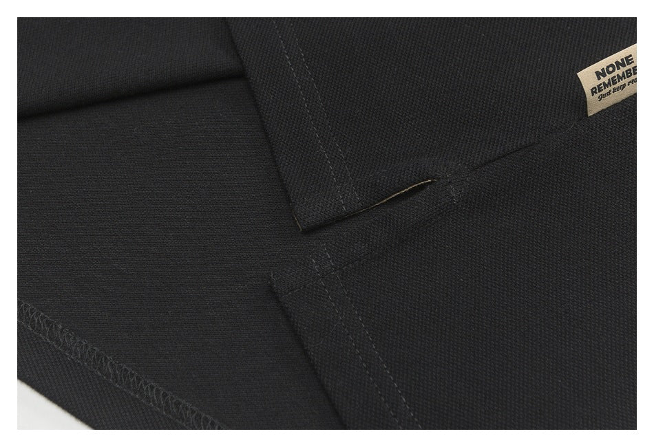 Close-up of black polo shirt seams and stitching, with part of a beige printed label at the edge.