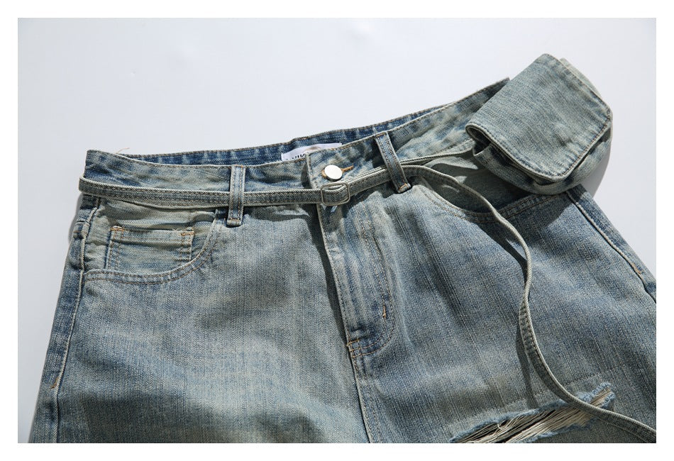 Upper front of faded blue jeans laid flat, with a belt, attached pouch, and frayed distressing near the hem of the crop.