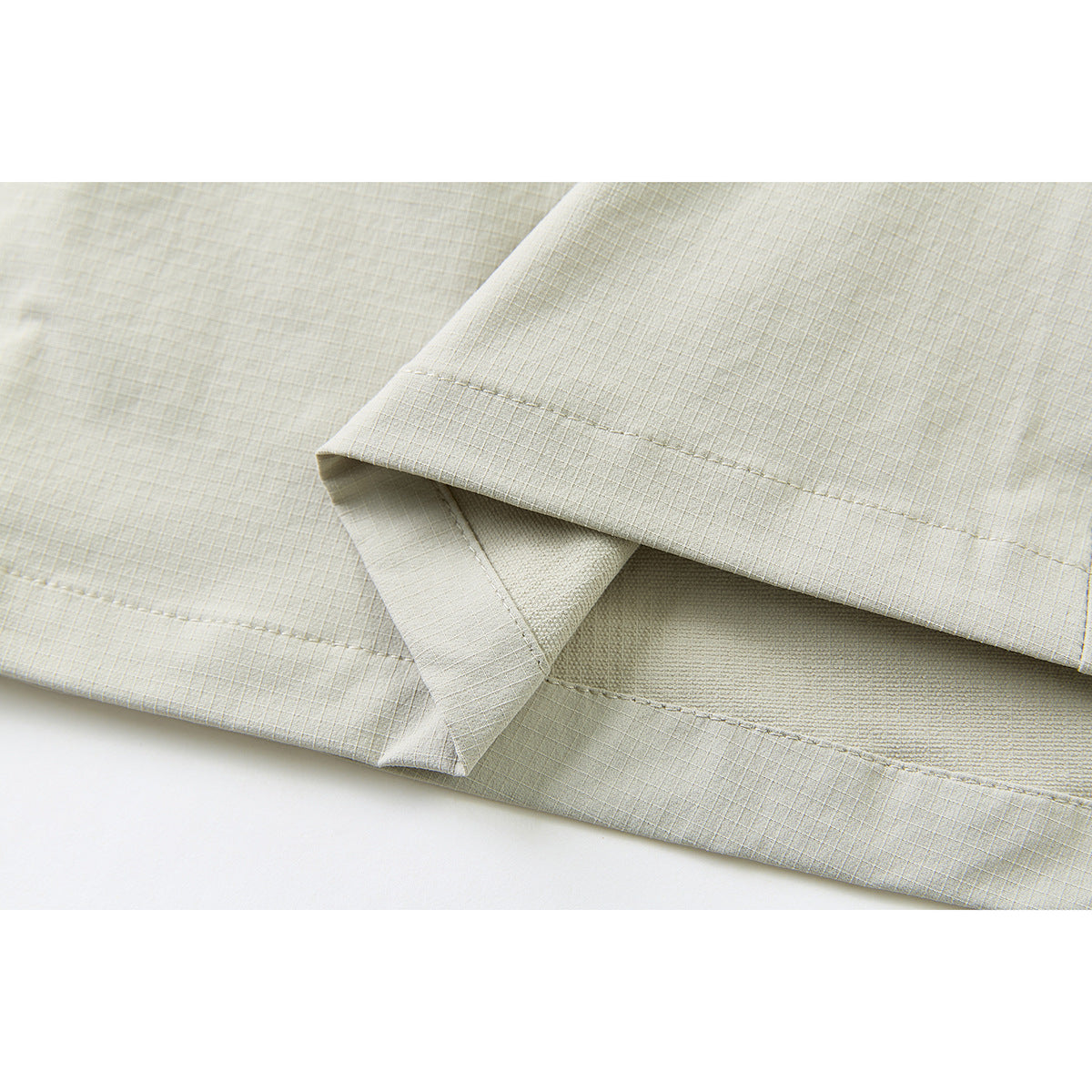 Close-up of the stitched hem and folded edge of pale sage pants.