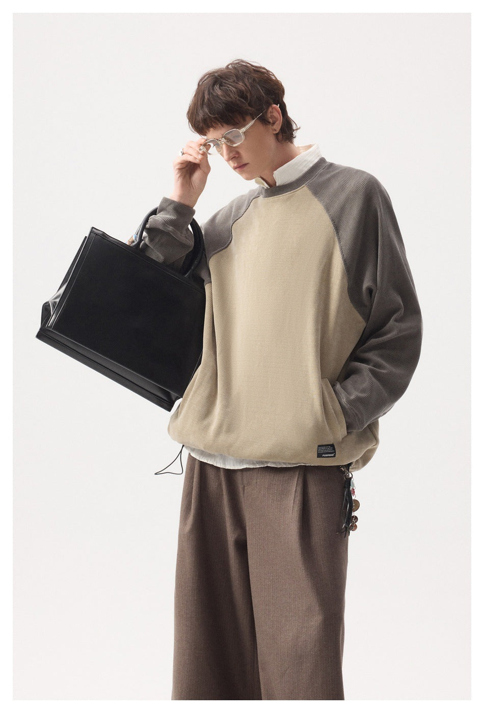 Model wearing a beige pullover with gray raglan sleeves and a drawcord hem.