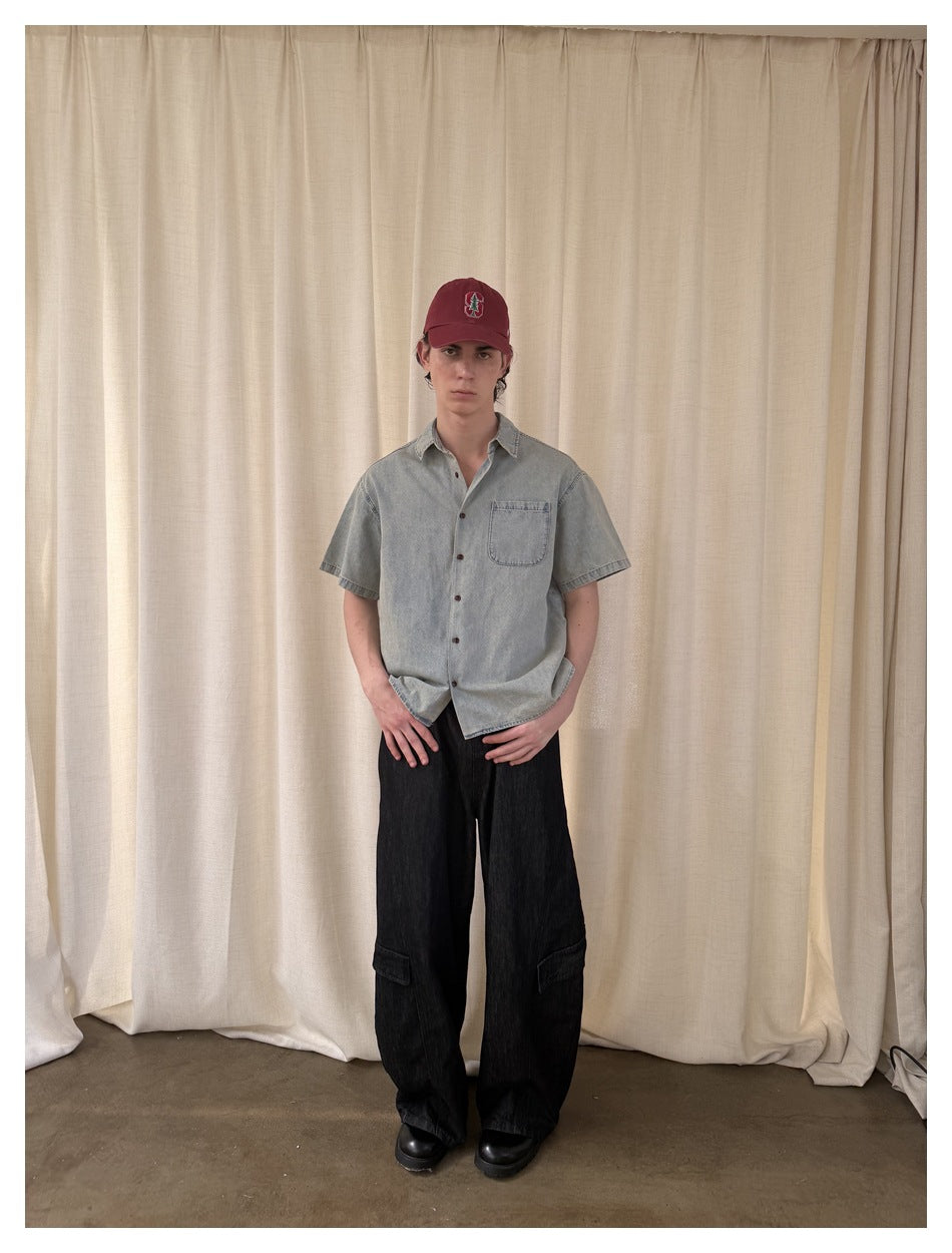 Full-length view of a model wearing a pale washed-blue short-sleeve button-up shirt and loose black pants.