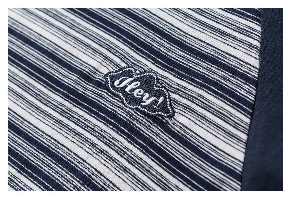 Close-up of a white embroidered script emblem on the navy-and-white striped chest of a T-shirt.