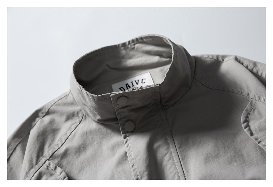 Close-up of the gray jacket’s stand collar, snap-button placket, stitching, and sewn neck label.