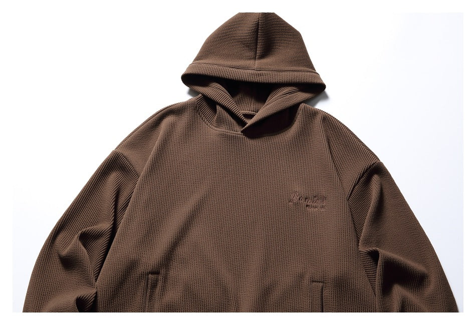 Front view of a brown textured pullover hoodie with a hood, kangaroo pocket and small chest embroidery.