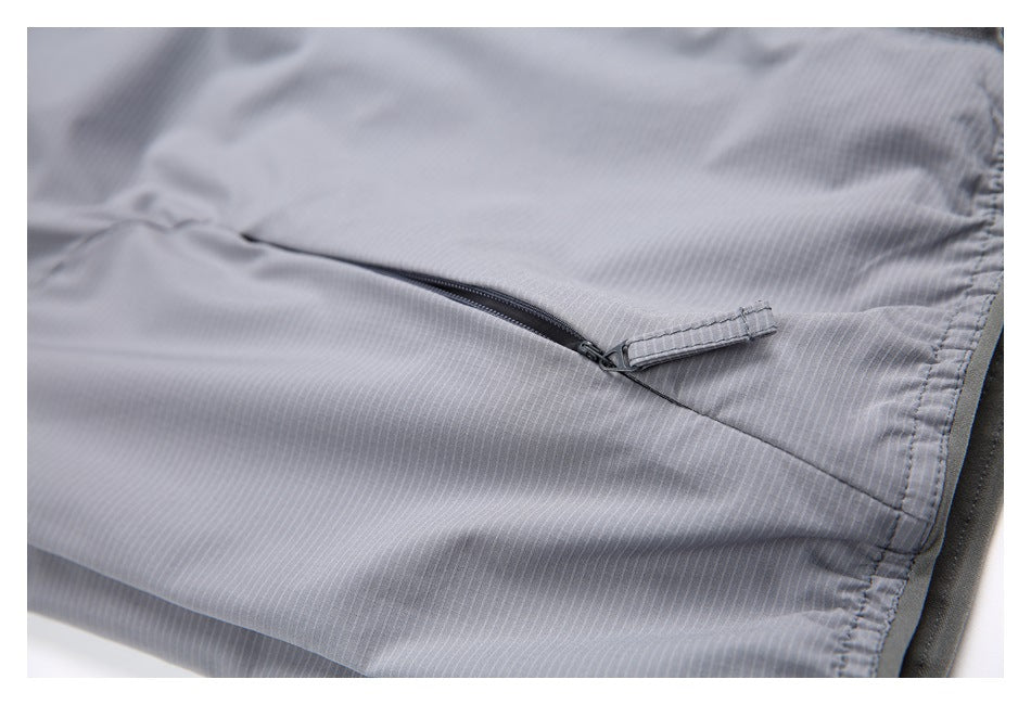 Close-up of a slanted zippered pocket on gray vest fabric.