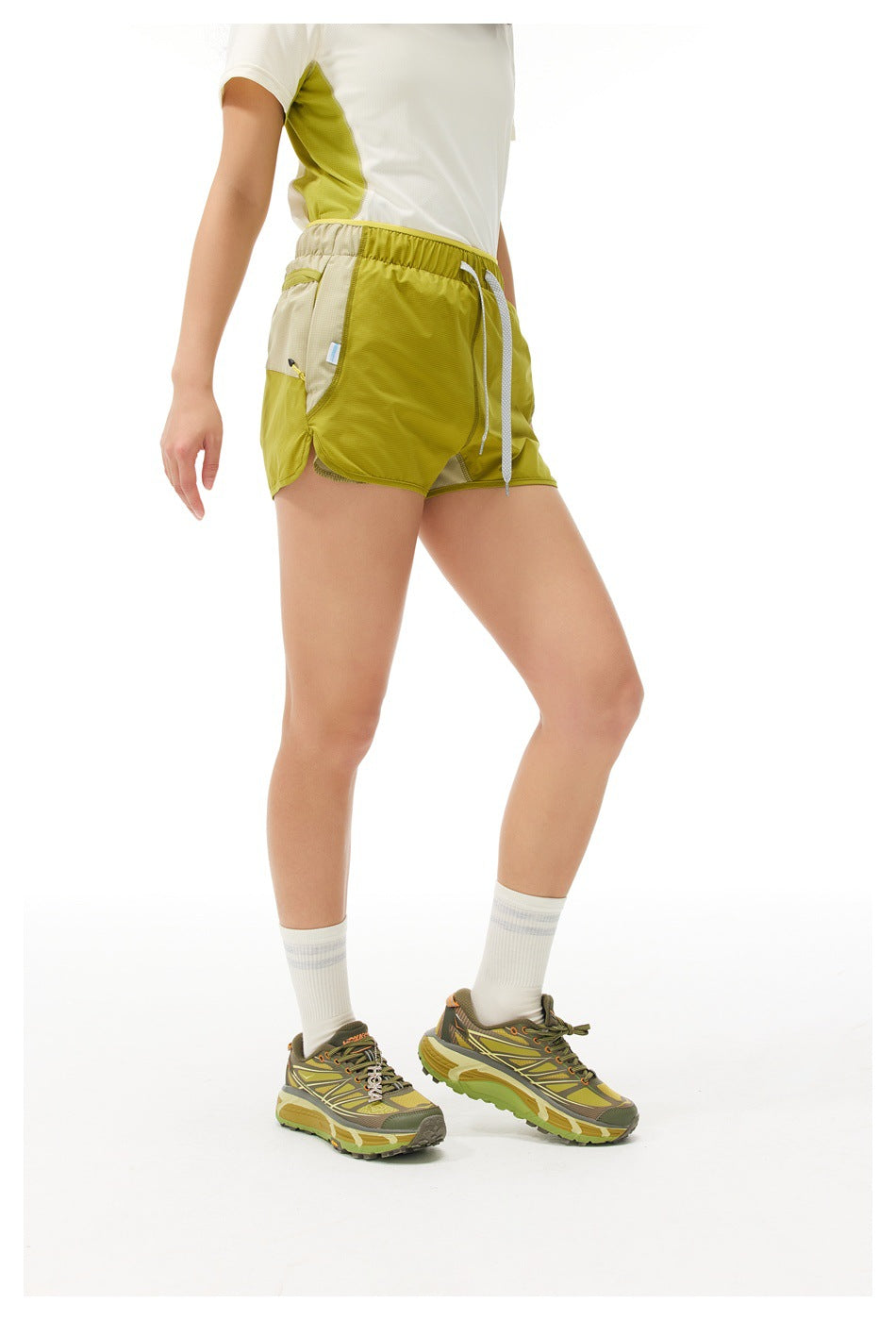 Angled front view of a model wearing lime-green and beige color-block running shorts with white drawstrings.
