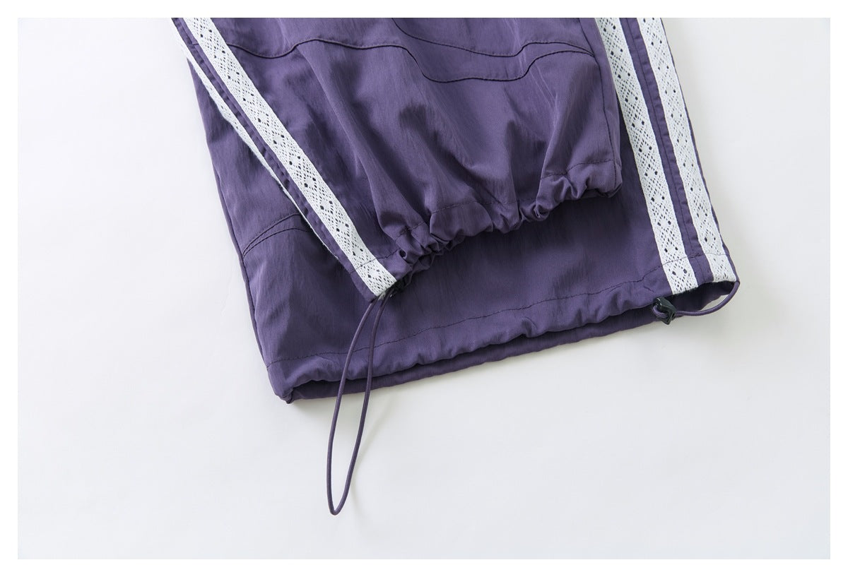 Close-up of purple pants hem with gathered elastic, an adjustable drawcord, and white lace side stripes.