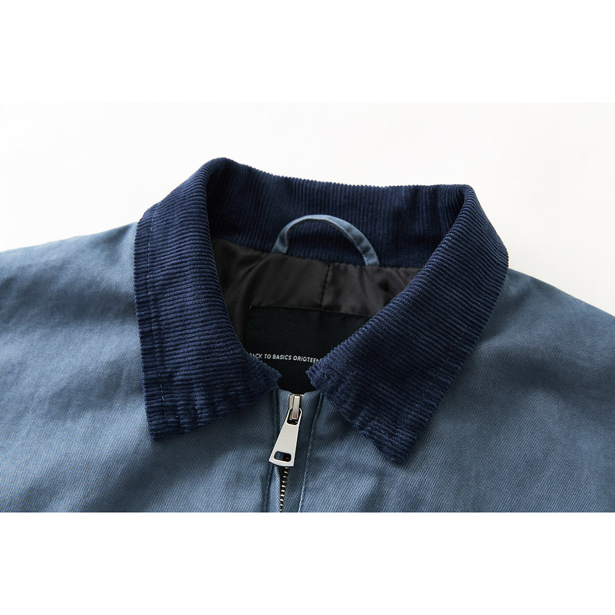 Close-up of a blue jacket's dark ribbed collar, neck label, and silver front zipper.
